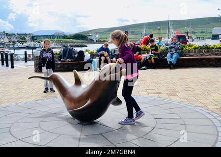 I bambini giocano sulla statura di ottone di fungie il delfino nella città di dingle, Irlanda. Foto Stock