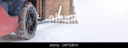 Ruota del trattore con catena. Trattore o caricatore su una strada sdrucciolevole e innevata. I caricatori si azionano sulla neve con catene antislittamento. Foto Stock