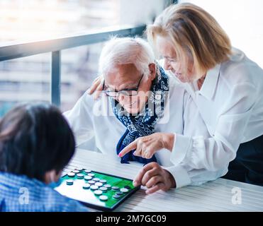 sfocatura selettiva. nonni che si divertono mentre giocano a un gioco da tavolo con il loro nipote. il nonno ride come sua moglie indica il gioco. Foto Stock