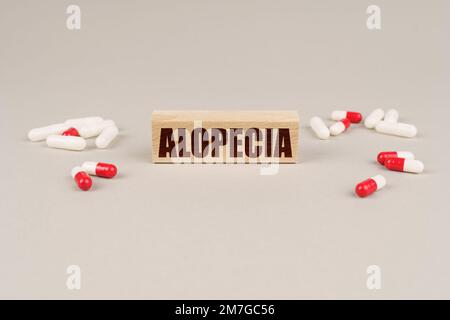 Concetto medico. Su una superficie grigia sono presenti compresse, capsule e una lastra di legno con l'iscrizione Alopecia Foto Stock