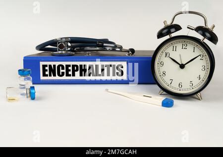 Concetto medico. Su una superficie bianca, un termometro, ampolle, uno stetoscopio, una sveglia e una cartella con l'iscrizione - encefalite Foto Stock