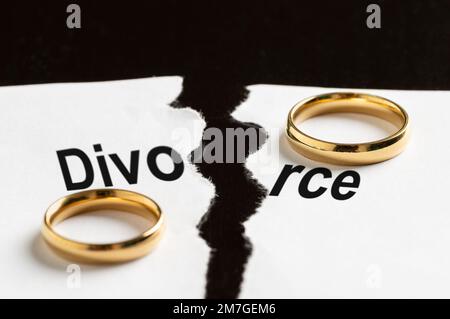 Primo piano di un documento di rottura con la parola divorzio e due anelli di nozze su un tavolo nero Foto Stock