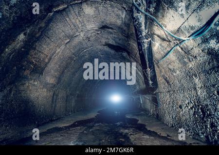 Acque fognarie in un grande tunnel sotterraneo. All'interno di un tunnel di corridoio fognario urbano scuro con luce alla fine Foto Stock