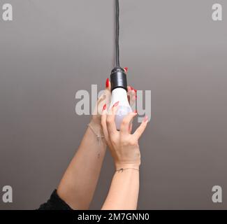 risparmio energetico. Una donna installa una lampada a LED. lampadina elettrica in mano Foto Stock