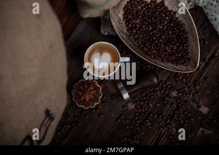 Caffè aromatico appena preparato su uno sfondo di chicchi di caffè e biscotti cremosi. Atmosfera da caffè Foto Stock