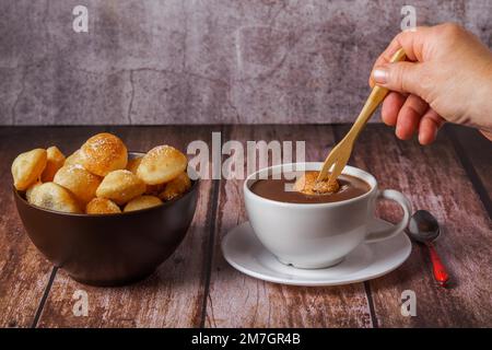 Donna che spalma una ciambella zuccherata con una forchetta di legno su una cioccolata calda in una tazza bianca Foto Stock