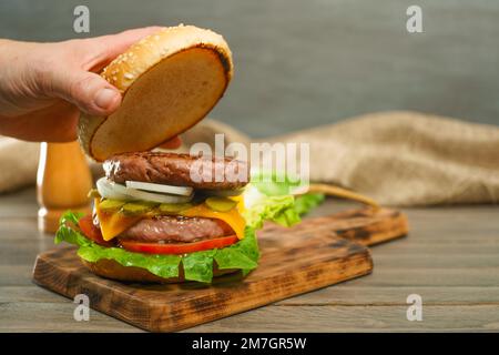 Primo piano delle mani di una donna che apre il panino di un hamburger completo di due pezzi di carne su un asse di legno Foto Stock