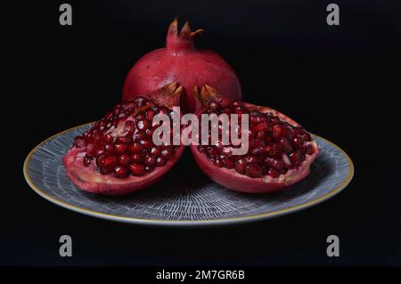 Melograno fresco si apre su di un piatto giallo con fondo nero su di un piatto con fondo nero Foto Stock