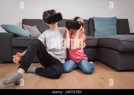 I bambini stupiti che usano gli occhiali per la realtà virtuale che giocano nel salotto di casa. Fratello e sorella Foto Stock