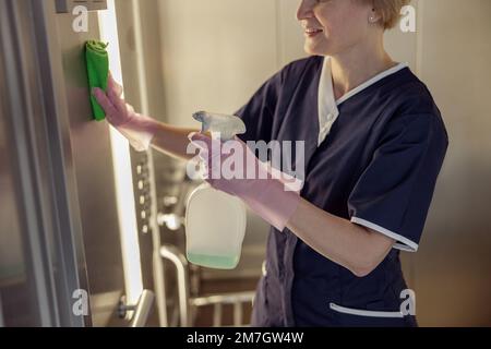 Primo piano della cameriera che indossa uniforme e guanti pulizia ascensore con detergente e straccio Foto Stock