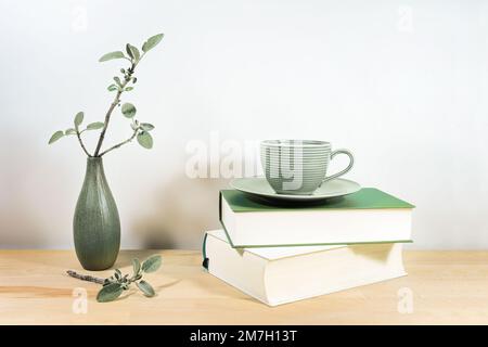 Scrivania in legno o tavolo con libri, una tazza da tè verde e salvia ramoscelli in un piccolo vaso di ceramica contro una parete bianca grigia, spazio copia, fuoco selezionato, stretto Foto Stock