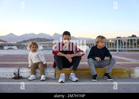 Tre fratelli seduti fuori su un marciapiede e Buon divertimento. Foto Stock