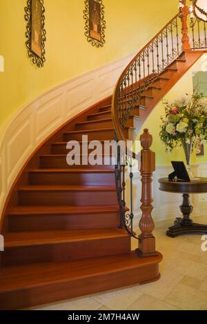 Scala ricurva in legno marrone e verniciata nel corridoio all'interno di un'elegante casa in stile cottage. Foto Stock