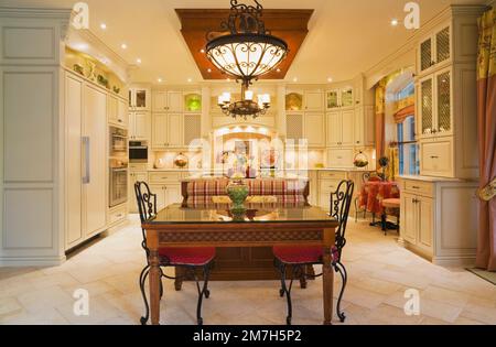 Lampadari illuminati sopra il tavolo della colazione e sedie rivestite rosse in cucina all'interno di un'elegante casa in stile cottage. Foto Stock