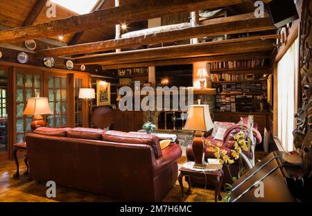 Divani in pelle Borgogna e caminetto in pietra nella camera per famiglie all'interno di una casa in legno in stile cottage delle 1800. Foto Stock