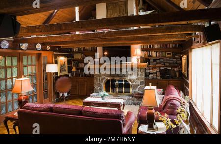 Divani in pelle Borgogna e caminetto in pietra nella camera per famiglie all'interno di una casa in legno in stile cottage delle 1800. Foto Stock