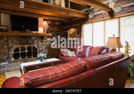 Divani in pelle Borgogna e caminetto nella camera per famiglie all'interno di una casa in legno costruita in stile cottage anni '1800. Foto Stock