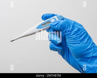 Mano in guanto blu con termometro digitale su sfondo bianco. Operatore medico che indossa guanti protettivi per il controllo del termometro medico. Foto Stock