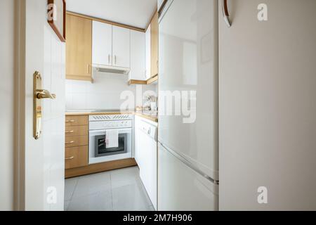 cucina con armadi bianchi combinati con legno con accesso attraverso uno stretto corridoio Foto Stock