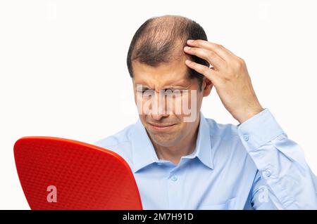Uomo di mezza età sconvolto con alopecia guardando specchio, perdita di capelli concetto Foto Stock