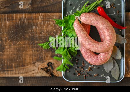 Anelli di salsiccia. Anelli di salsiccia fatti in casa crudi, prezzemolo fresco, peperoncino rosso in un piatto nero su un tavolo di legno scuro. appetitosi prodotti di carne con Foto Stock