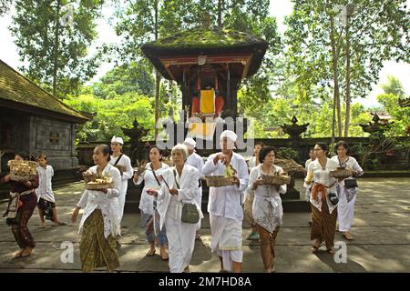 Un prete balinese sta in piedi davanti alle donne di un clan che stanno portando offerte spirituali durante una processione per onorare e purificare gli spiriti dei loro ultimi membri della famiglia, in un tempio situato nel complesso del tempio di Besakih, sul pendio del Monte Agung a Karangasem, Bali, Indonesia. Foto Stock