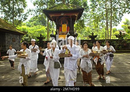 Un prete balinese sta in piedi davanti alle donne di un clan che stanno portando offerte spirituali durante una processione per onorare e purificare gli spiriti dei loro ultimi membri della famiglia, in un tempio situato nel complesso del tempio di Besakih, sul pendio del Monte Agung a Karangasem, Bali, Indonesia. Foto Stock