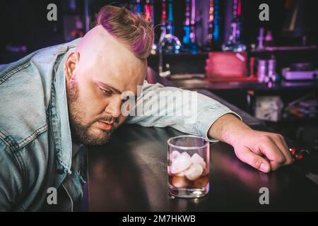 un brutale uomo ubriaco con un cocktail alcolico in un bicchiere. Il concetto di cattive abitudini e dipendenza da alcol. Foto Stock