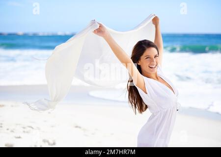 Estate style.A bella giovane donna sulla spiaggia che tiene una sciarpa bianca thats soffiare nel vento. Foto Stock