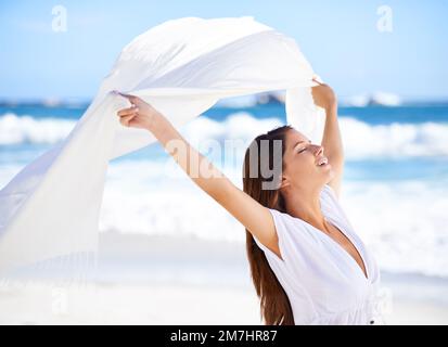 Bellezza nella brezza. Una bella giovane donna sulla spiaggia che tiene una sciarpa bianca che soffia nel vento. Foto Stock