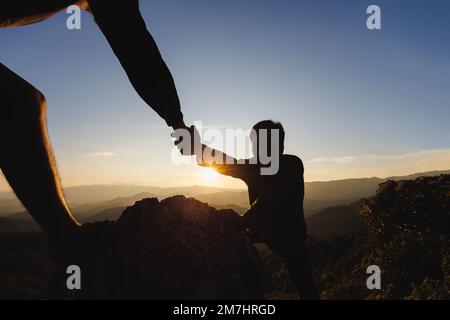 Gli escursionisti che si arrampicano sulla scogliera di montagna e uno di loro dà mano d'aiuto. Persone che aiutano e, concetto di lavoro di squadra. Foto Stock