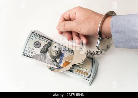 Mano con manette e dollari USA su sfondo bianco. concetto di dipendenza dal denaro. La criminalità in ambito finanziario. uomo d'affari criminale, corrotto Foto Stock