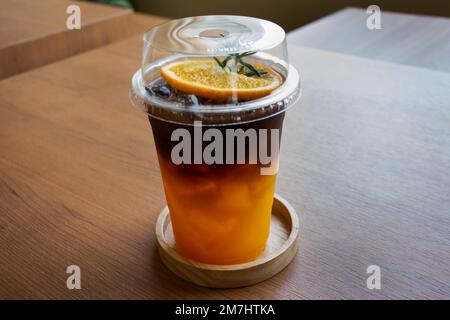 Caffè nero espresso servito con succo d'arancia e ghiaccio freddo in una tazza di vetro di plastica per i viaggiatori thailandesi mangiare e bevande nella caffetteria classica r Foto Stock