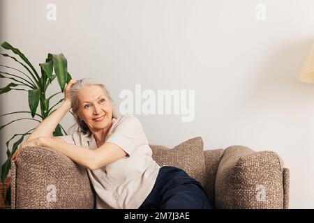 Donna anziana pensiva che si rilassa a casa seduta in una poltrona Foto Stock