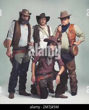 Nessuno si è mai preoccupato di chiedere come è venuta ad essere nella banda... Una banda di fuorilegge in piedi isolati sul grigio mentre si guarda duro. Foto Stock
