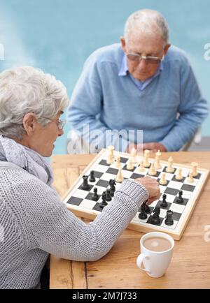 Là..il mio cavaliere prende il vostro vescovo. Una coppia anziana che gioca a scacchi insieme sul patio. Foto Stock