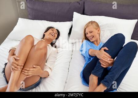 Condividere uno scherzo. due giovani amici ridendo sdraiati su un letto. Foto Stock