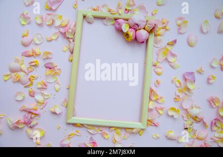 Petali di rosa, boccioli di rosa e cornice di legno vuota su sfondo rosa chiaro. Giacitura piatta, spazio di copia. Festa della mamma, San. San Valentino, marzo 8 concetto. In alto Foto Stock