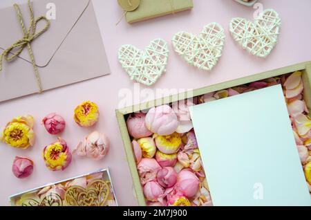 Composizione per San Valentino. Piatto di cuori bianchi, scatole regalo fatte a mano, carta da artigianato, busta, boccioli di rosa su sfondo rosa. Vista dall'alto, spazio di copia. Foto Stock