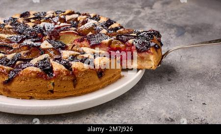 Vista panoramica pezzo di crostata di prugna sulla lama della spalla e torta sul piatto, primo piano, messa a fuoco selettiva Foto Stock