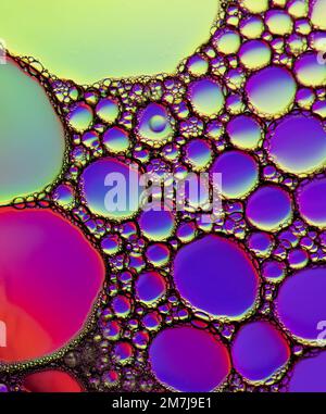 Motivi colorati di diffrazione della luce formati da goccioline di olio che galleggiano sull'acqua sopra uno sfondo colorato Foto Stock