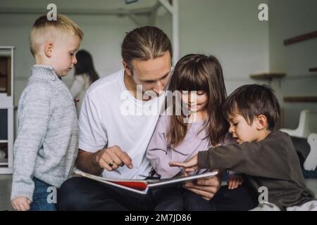 Libro di storia di lettura dell'insegnante con gli studenti nel centro di assistenza per bambini Foto Stock