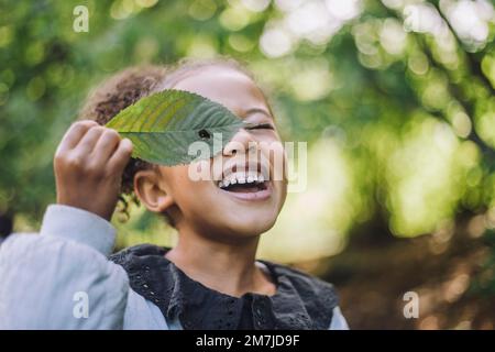 Ragazza sorridente che guarda attraverso il foro in foglia verde Foto Stock