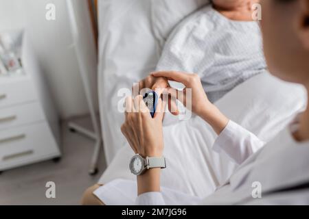 Vista ritagliata del medico che indossa il pulsossimetro sul dito del paziente in clinica, immagine stock Foto Stock