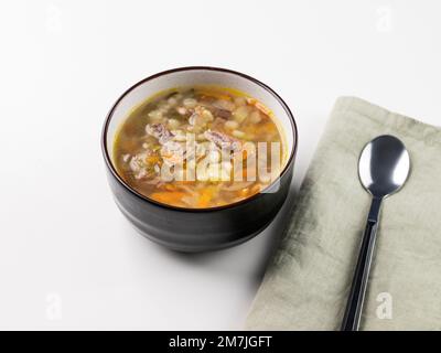 Zuppa tradizionale russa con cetrioli sottaceto. Sottaceti con orzo perlato e carne su fondo bianco con tovagliolo e cucchiaio. Foto Stock