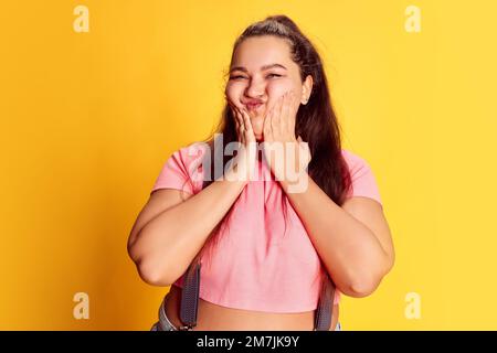 Ritratto di giovane donna sovrappeso in abiti casual luminosi che si posano su sfondo giallo vivo studio. Faccia divertente Foto Stock