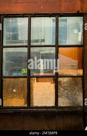 Primo piano di una vecchia finestra intemprata con vernice sbucciata e vetro appannato in un ambiente urbano Foto Stock