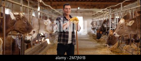 Lavoratore maschile con un attrezzo in piedi in un fienile con mucche Foto Stock