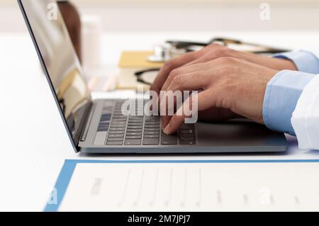 Foto di un medico maschio irriconoscibile che lavora sul suo computer portatile mentre è seduto in ufficio in ospedale Foto Stock