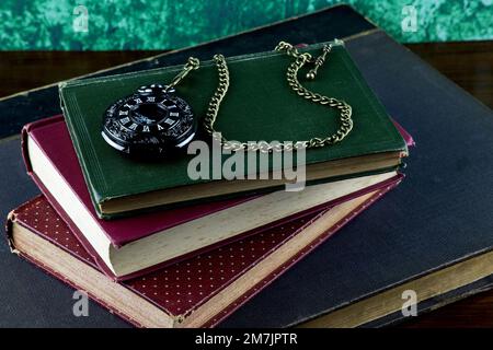 Orologio da tasca nero e vecchi libri su un tavolo in legno Foto Stock